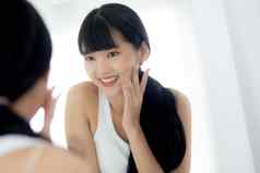 美丽的脸年轻的亚洲女人快乐微笑触摸脸颊镜子迷人的化妆美面部女孩护肤品化妆品治疗皮肤护理健康的概念