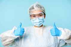 肖像微笑亚洲护士医生穿个人保护设备显示拇指推荐站蓝色的背景