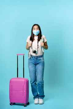 热情的女孩旅行者亚洲旅游背包手提箱穿医疗脸面具兴奋旅程假期旅行站蓝色的背景