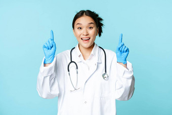 热情的亚洲医生女医生指出手指微笑显示广告展示促销蓝色的背景