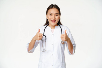 微笑亚洲女医生穿医疗袍显示拇指很高兴推荐健康产品站白色背景