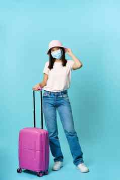 完整的长度肖像快乐亚洲女人旅行者手提箱穿医疗脸面具科维德流感大流行假期蓝色的背景