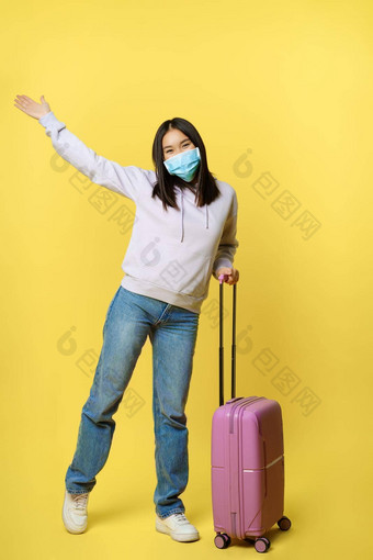 完整的长度拍摄快乐朝鲜文女孩旅游假期摆姿势手提箱医疗脸面具享受旅行概念旅游流感大流行医疗保健