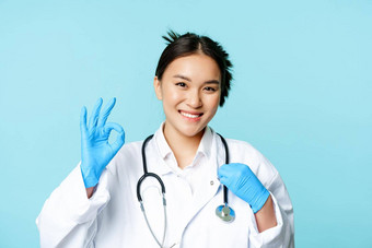微笑亚洲医生女医生触碰听诊器显示标志批准蓝色的背景