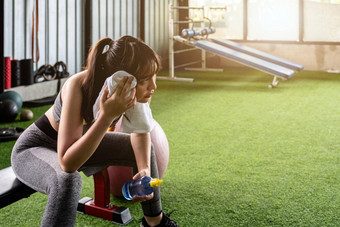 年轻的亚洲女人喝水擦拭汗水毛巾吉尔采取打破锻炼健身房