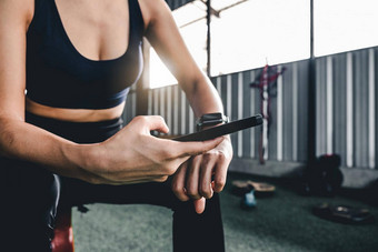 体育运动女人休息锻炼智能手表连接智能手机锻炼应用程序在室内健身房背景健康体育运动概念