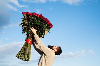 有胡子的男人。红色的玫瑰花束情人节一天礼物爱英俊的男人。背景天空礼物情人节一天