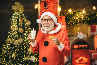 肖像有胡子的有趣的男人。圣诞老人服装圣诞老人老人享受饼干牛奶左圣诞节夏娃牛奶饼干圣诞老人老人圣诞老人挑选饼干