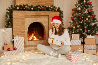 美丽的年轻的女人黑暗头发微笑持有节日礼物手坐着壁炉圣诞节树快乐女孩穿着圣诞老人他温暖的毛衣袜子
