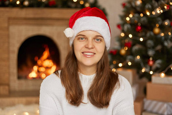 肖像美丽的高加索人女模型穿圣诞老人他白色毛衣摆姿势首页壁炉x-mas树背景夫人<strong>露出</strong>牙齿的微笑相机