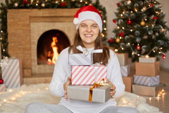 微笑女孩给圣诞节礼物首页持有礼物盒子手坐着地板上<strong>装饰</strong>生活房间壁炉x-mas树背景