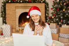 高加索人夫人移动PC视频调用沟通装修圣诞节树白色房间首页壁炉微笑女孩快乐庆祝一年