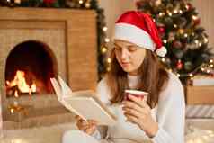 女人休息杯热喝书壁炉圣诞节树集中页面支出休闲时间穿节日他白色针织毛衣