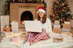 美丽的年轻的女圣诞老人他庆祝圣诞节一年首页移动PC摆姿势背景圣诞节树壁炉现在盒子灯
