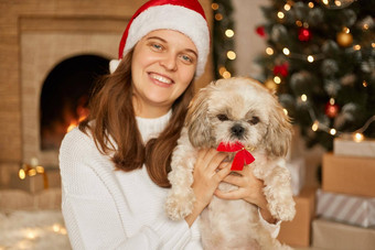 快乐的年轻的夫人享受时间宠物摆姿势生活房间x-mas树壁炉女人穿圣诞老人老人他白色跳投圣诞节大气