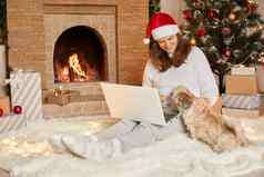快乐女孩红色的他坐着移动PC坐着可爱的狗圣诞节树灯壁炉礼物节日房间女北京人的小狗快乐