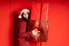 年轻的女人圣诞老人条款他持有大礼物站红色的墙快乐女圣诞节他盒子礼物概念假期礼物好情绪