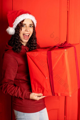 年轻的女人圣诞老人老人他持有大礼物站红色的墙快乐女圣诞节他盒子礼物概念假期礼物好情绪