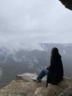 年轻的女人坐着边缘悬崖多雾的多云的天气女旅游享受壮观的视图自然坐着高岩石