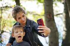 年轻的妈妈。儿子需要自拍微笑年轻的女人长头发孩子自拍智能手机公园