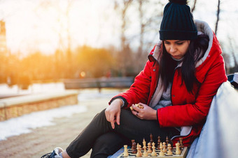 年轻的女人冬天衣服戏剧国际象棋坐着板凳上城市公园女黑色的帽国际象棋<strong>木皮</strong>尤多云的天气