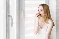 美丽的青少年女孩白色衣服吃苹果窗口