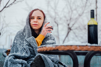 年轻的女人坐着院子里喝红色的酒雪天气女包装灰色格子坐着街酒精冬天季节