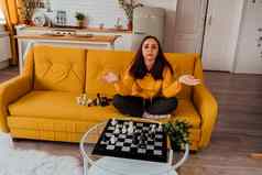 年轻的心烦意乱女人玩国际象棋坐着沙发陷入困境的女戏剧逻辑董事会游戏房间