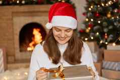 高加索人女人收到惊喜礼物圣诞节一天开放现在盒子微笑幸福的庆祝活动摆姿势模糊圣诞节树壁炉背景