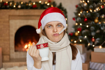 年轻的生病了女人圣诞老人他包装围巾测量温度持有杯气候变暖喝相机生病的圣诞节假期摆姿势房间一年装饰