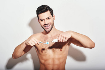 牙科护理年轻的黑头发的男人。站赤膊上阵<strong>挤压牙膏</strong>牙刷孤立的白色背景