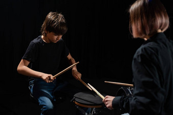 年轻的高加索人女人教男孩玩鼓工作室黑色的背景音乐学校学生