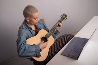 年轻的高加索人女人短金发女郎头发玩吉他看培训视频移动PC