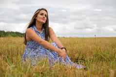 美丽的年轻的女人坐在草地花阳光明媚的夏天一天微笑