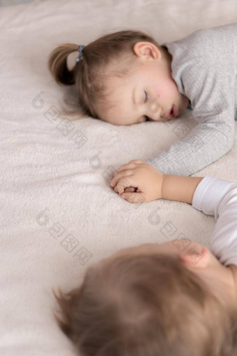 童年睡眠放松家庭生活方式概念年轻的孩子们年穿着白色米色紧身衣裤睡眠米色白色床上午餐持有手前视图