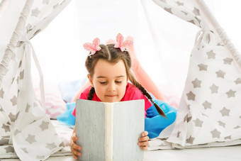 享受伟大的故事可爱的女孩阅读书坐着地板上帐篷
