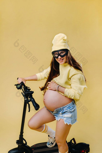怀孕了女孩黄色的衣服电踏板车孤立的黄色的背景