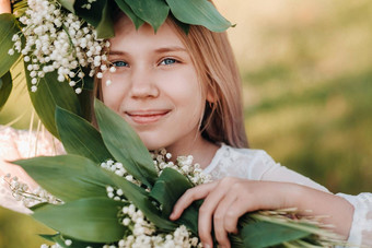 美丽的九岁的金发女郎女孩长头发长白色衣服持有花束百合谷花走自然公园夏天日落