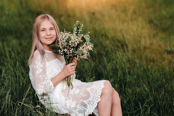 美丽的九岁的金发女郎女孩长头发长白色衣服持有花束<strong>百合</strong>谷花走自然公园夏天日落