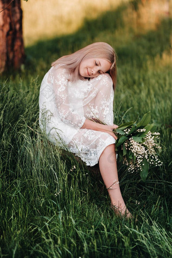 美丽的九岁的金发女郎长头发长白色衣服持有花束百合谷坐在石头公园夏天日落