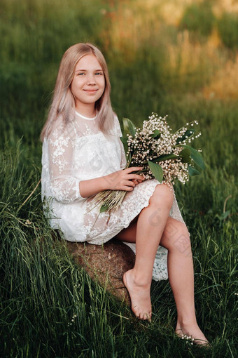 美丽的九岁的金发女郎女孩长头发长白色衣服持有花束百合谷花走自然公园夏天日落