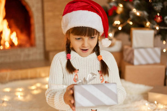 可爱的女孩子持有圣诞节礼物孩子有趣的圣诞节树生活房间惊讶孩子穿圣诞老人他白色毛衣现在盒子打开口