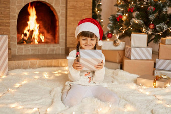 快乐孩子女孩圣诞节现在首页坐着温暖的地毯盒子手满意面部表达式摆姿势壁炉圣诞节树