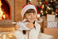 快乐女孩现在圣诞节夏娃坐着圣诞节树壁炉迷人的微笑孩子相机持有条纹礼物盒子弓