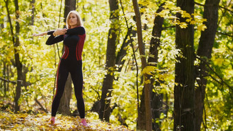 女人健身练习户外女伸展运动肩膀秋天森林苗条的女孩锻炼一边