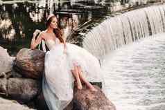 优雅的新娘白色衣服手套只脚坐着瀑布公园享受自然模型婚礼衣服手套自然公园白俄罗斯