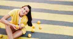 女孩持有柠檬手穿着黄色的衬衫短裤坐着黄色的行人穿越城市微笑柠檬情绪