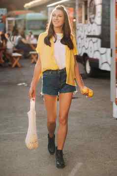 女孩黄色的衬衫短裤黑色的鞋子网柠檬柠檬汁走城市街女人鸡尾酒手