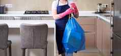 家庭主妇穿保护橡胶手套持有垃圾袋站厨房清洁服务概念