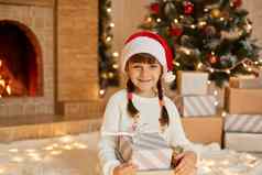 可爱的女孩子红色的他地板上首页圣诞节庆祝活动礼物女孩摆姿势礼物盒子微笑相机礼服白色跳投坐在壁炉圣诞节树
